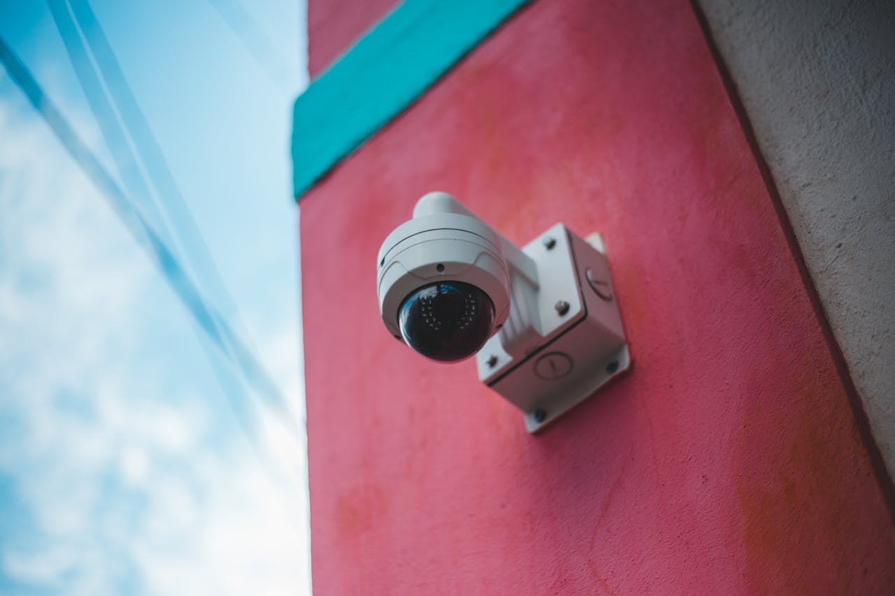 creative-01 A surveillance camera mounted on a vibrant pink and teal wall outdoors.